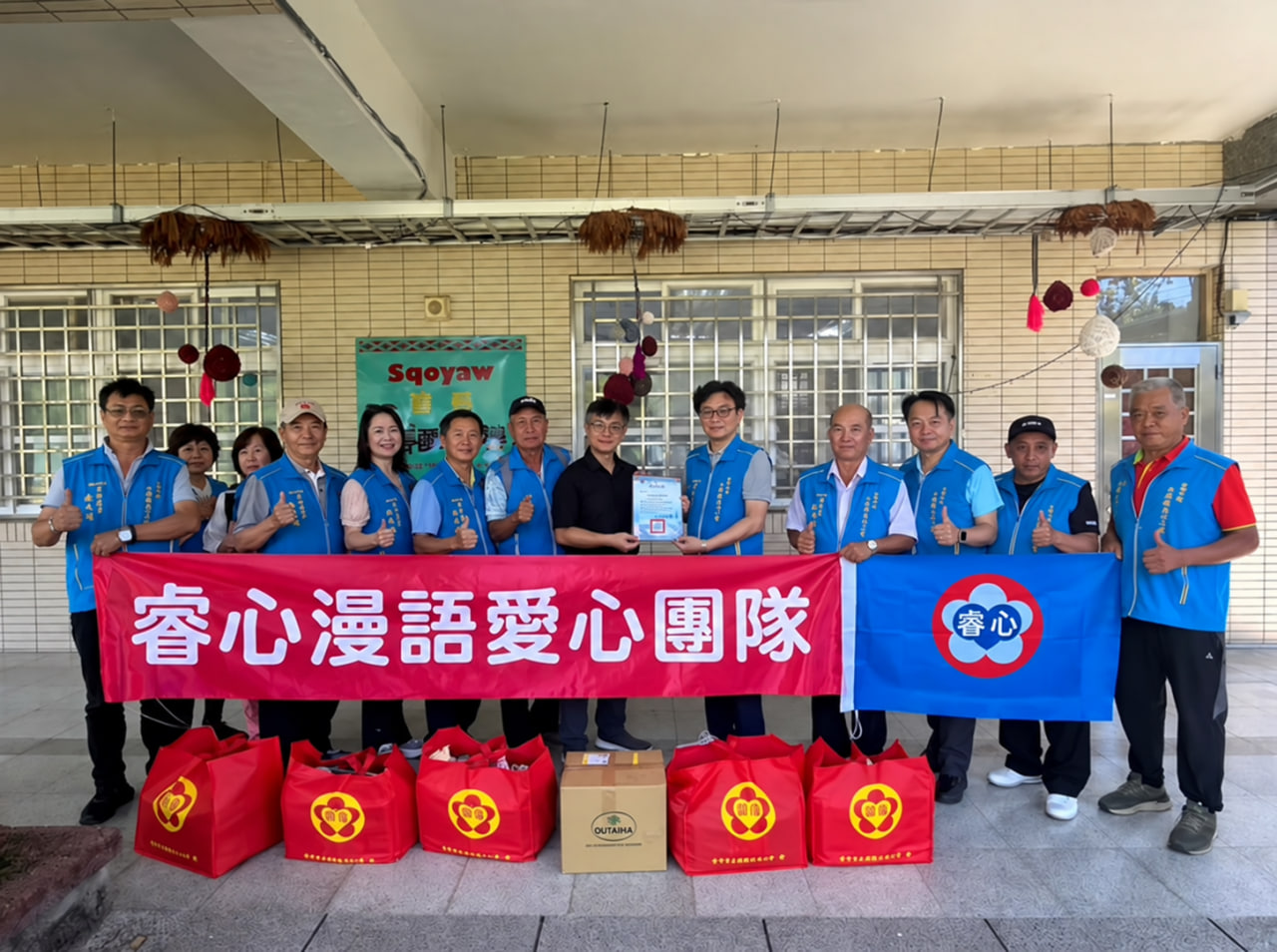 參與者手持「睿心漫語愛心團隊」布條合影，前方擺放物資。